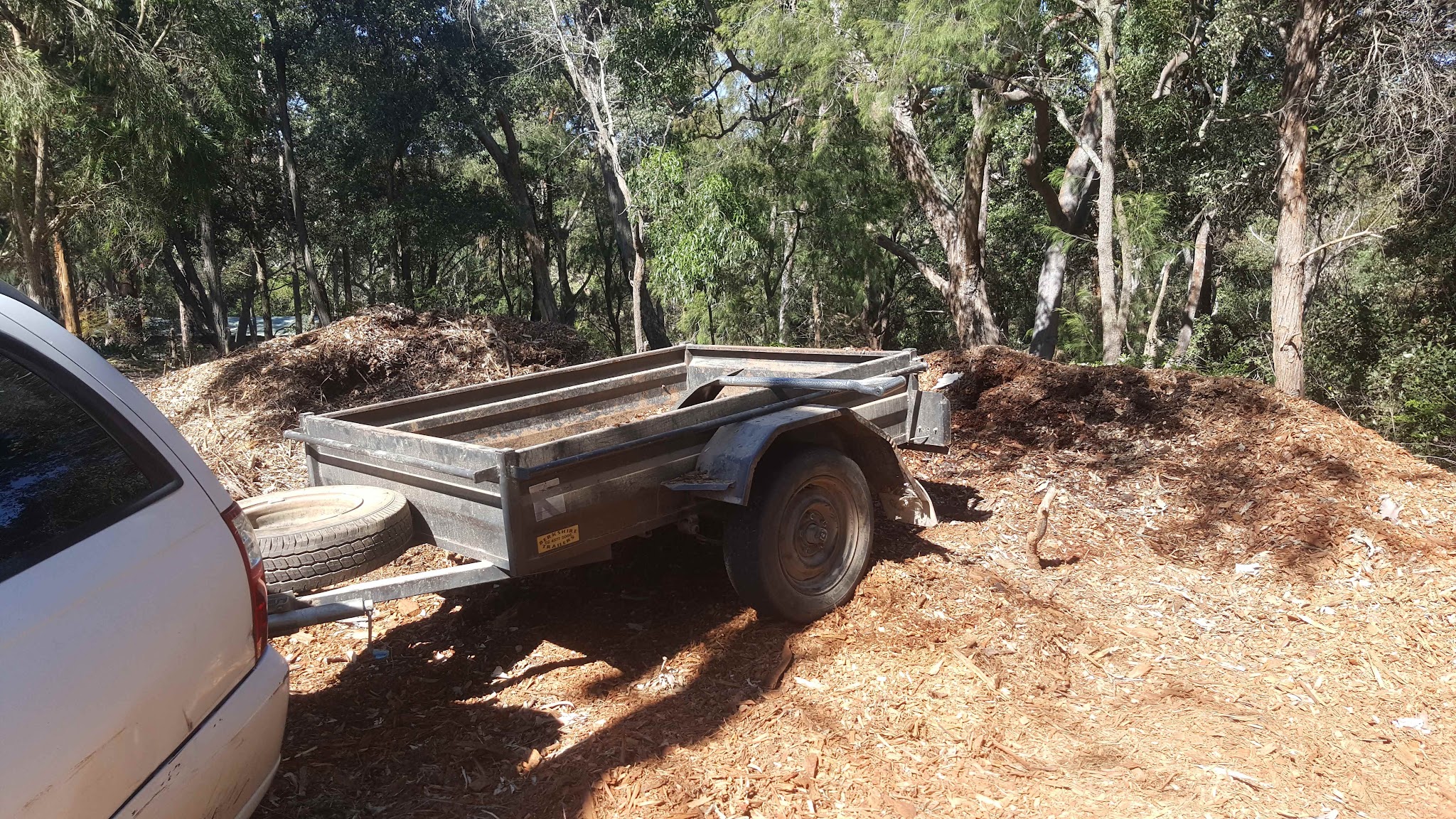 The work trailer parked at the mulch piles, hitched and ready for a green waste run.